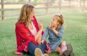 Mother and daughter sitting on grass using sign language
