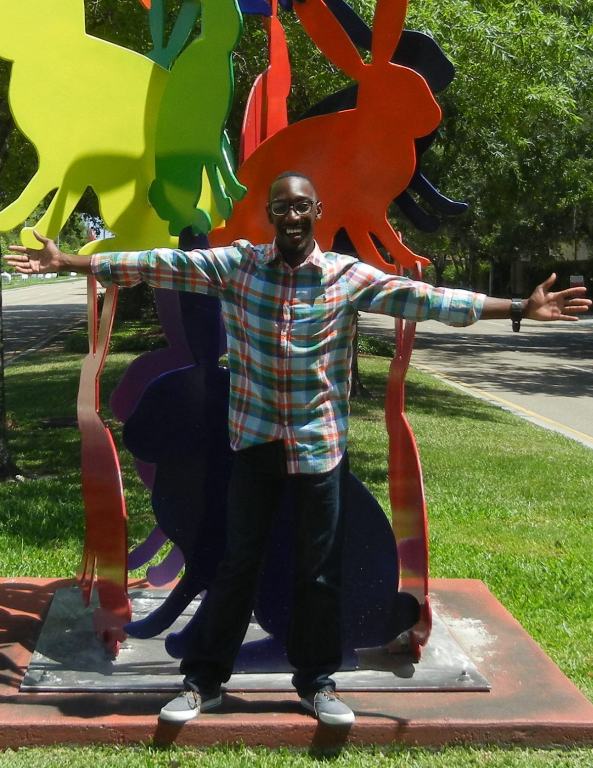 Man who is African American standing in front of art sculpture holding his arms wide open