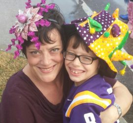 Mother wearing a pink fascinator hugging her elementary age son wearing a Mardi Gras hat