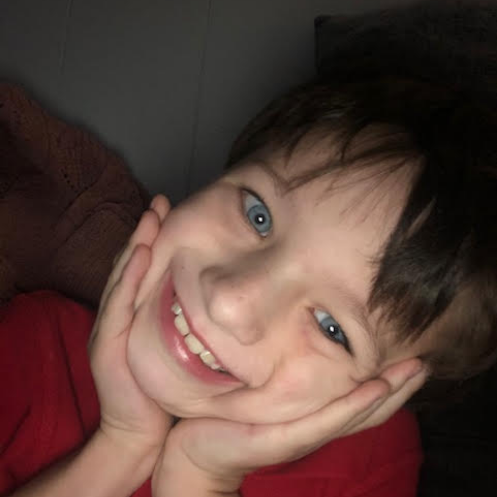 Boy with blue eyes and red shirt smiling holding his face with his hands