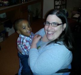 Woman with brown hair and glasses wearing a blue shirt holding African American baby boy