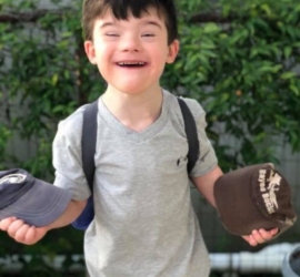 Elementary age boy with Down syndrome holding hats and smiling