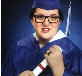 Teenage girl with brown hair and glasses in blue cap and gown holding her diploma