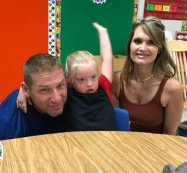 Girl with blonde hair who has Down syndrome at school with her mom and dad