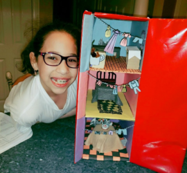 Young Spanish girl wearing glasses smiling next to her school project