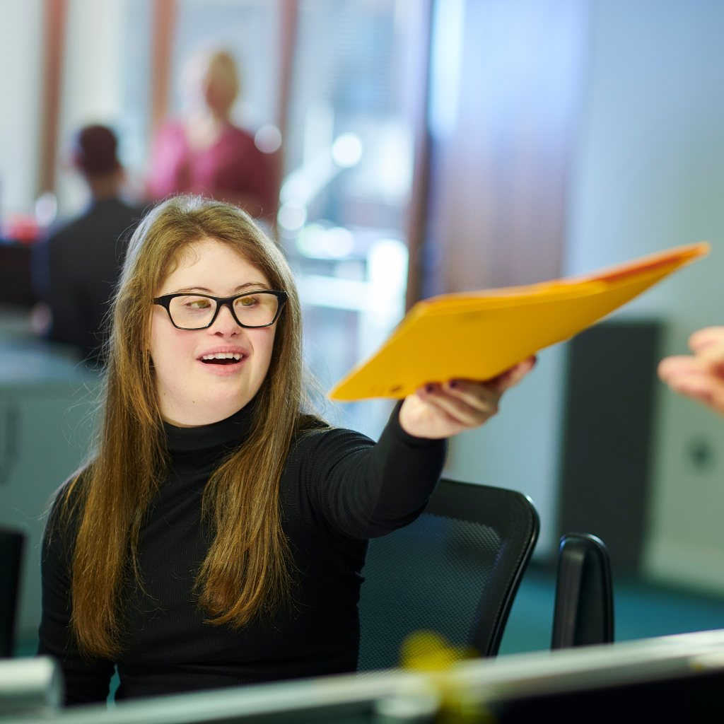 Adult woman with a disability wearing glasses holding a folder working in an office setting