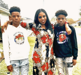 African American Mother and her two sons. Teen son wearing white hooded sweatshirt, Mother wearing bright colored dress with arms around her sons, Teen son wearing black sweatshirt