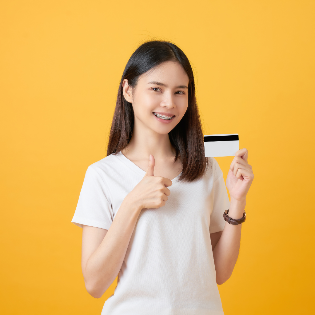 Asian teen girl holding a credit card in one hand and holding a thumbs up with the other hand
