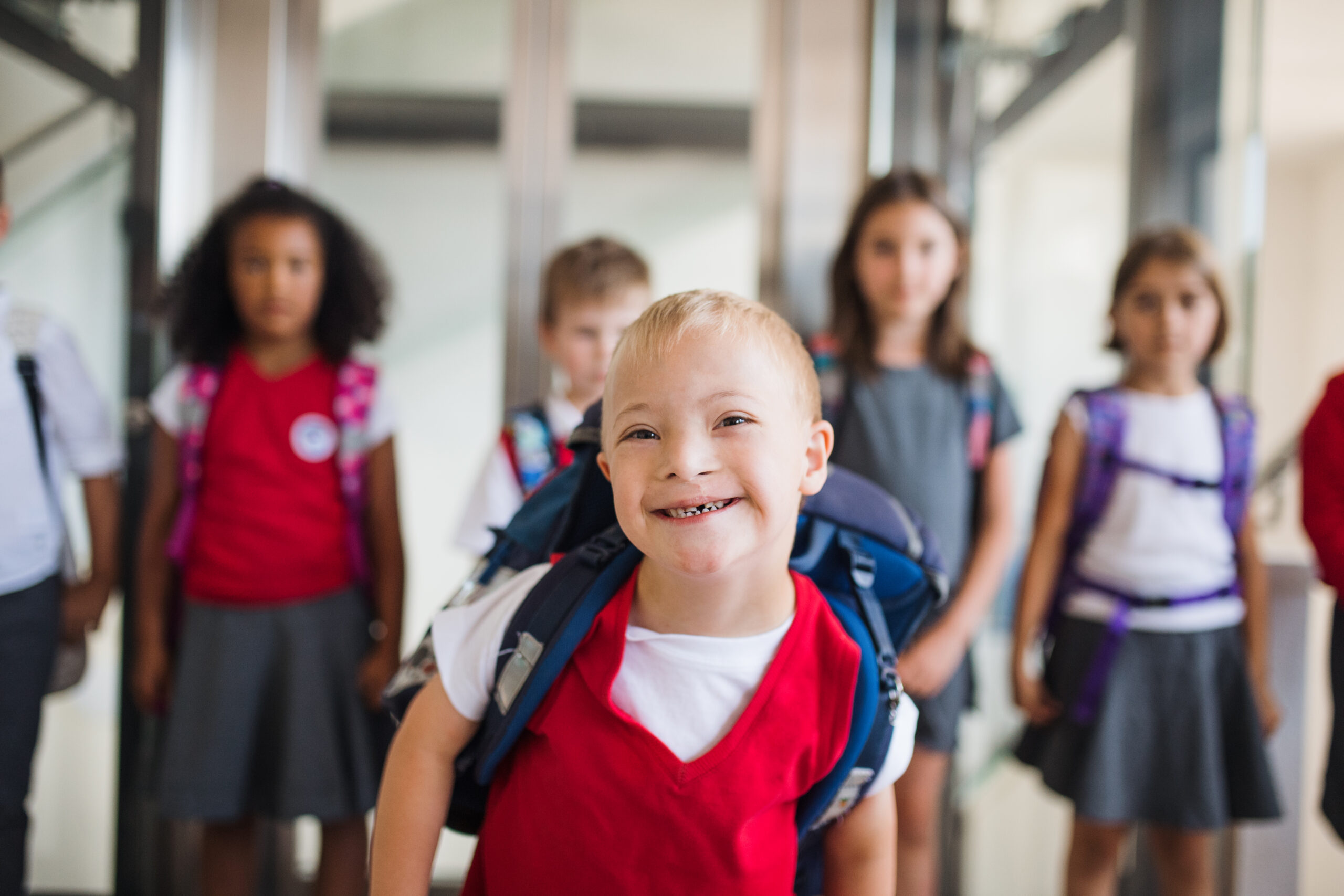 A school boy with down-syndrome and a group of children in corridor, walking.
