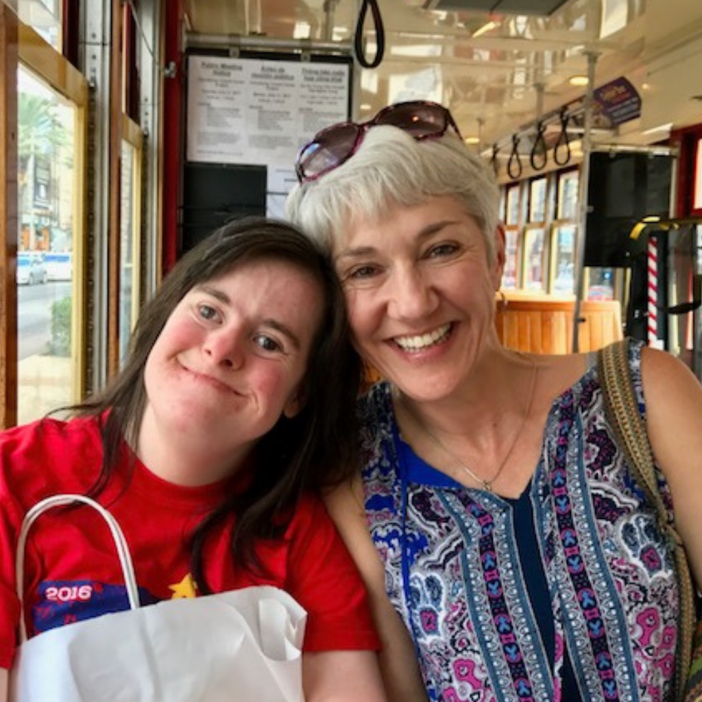 Adult woman with Down syndrome brown hair and red shirt holding a white bag with her mother riding a streetcar